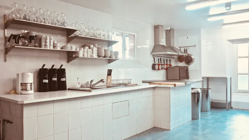 Cuisine professionnelle équipée avec ustensiles suspendus, étagères de vaisselle et grand plan de travail carrelé