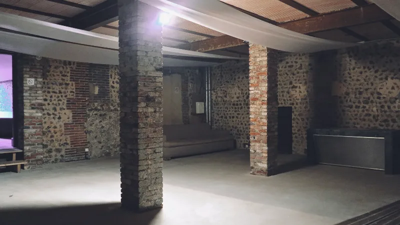 Vaste salle de réception voûtée en pierre et brique avec piliers apparents, pouvant accueillir des événements