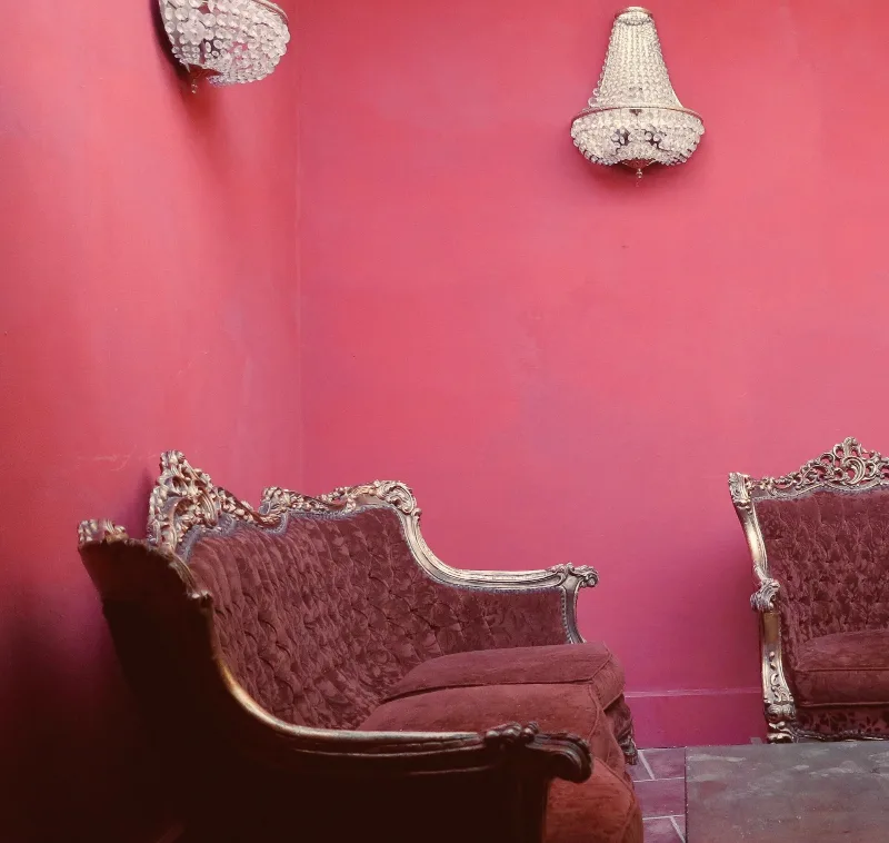 Salon cosy aux murs roses avec fauteuils baroques capitonnés et appliques en cristal