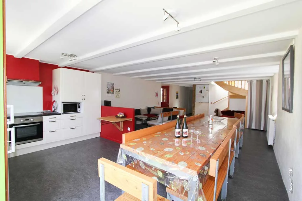 Gîte de groupe Gîte de Kerven à Arzano — Grande pièce de vie avec cuisine équipée, table longue et escalier, capacité 12 personnes
