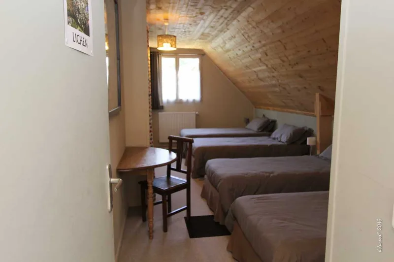 Chambre mansardée avec trois lits simples sous charpente en bois naturel