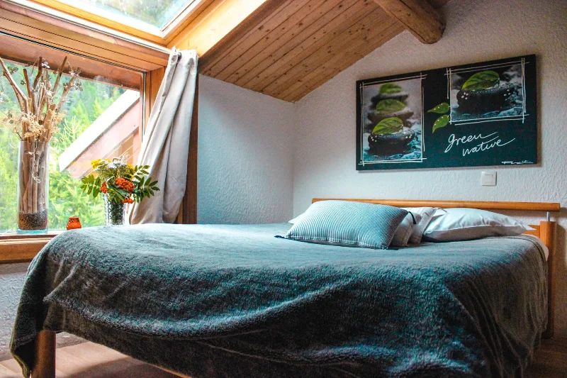 Chambre cosy sous charpente en bois avec lit double et fenêtre sur la nature