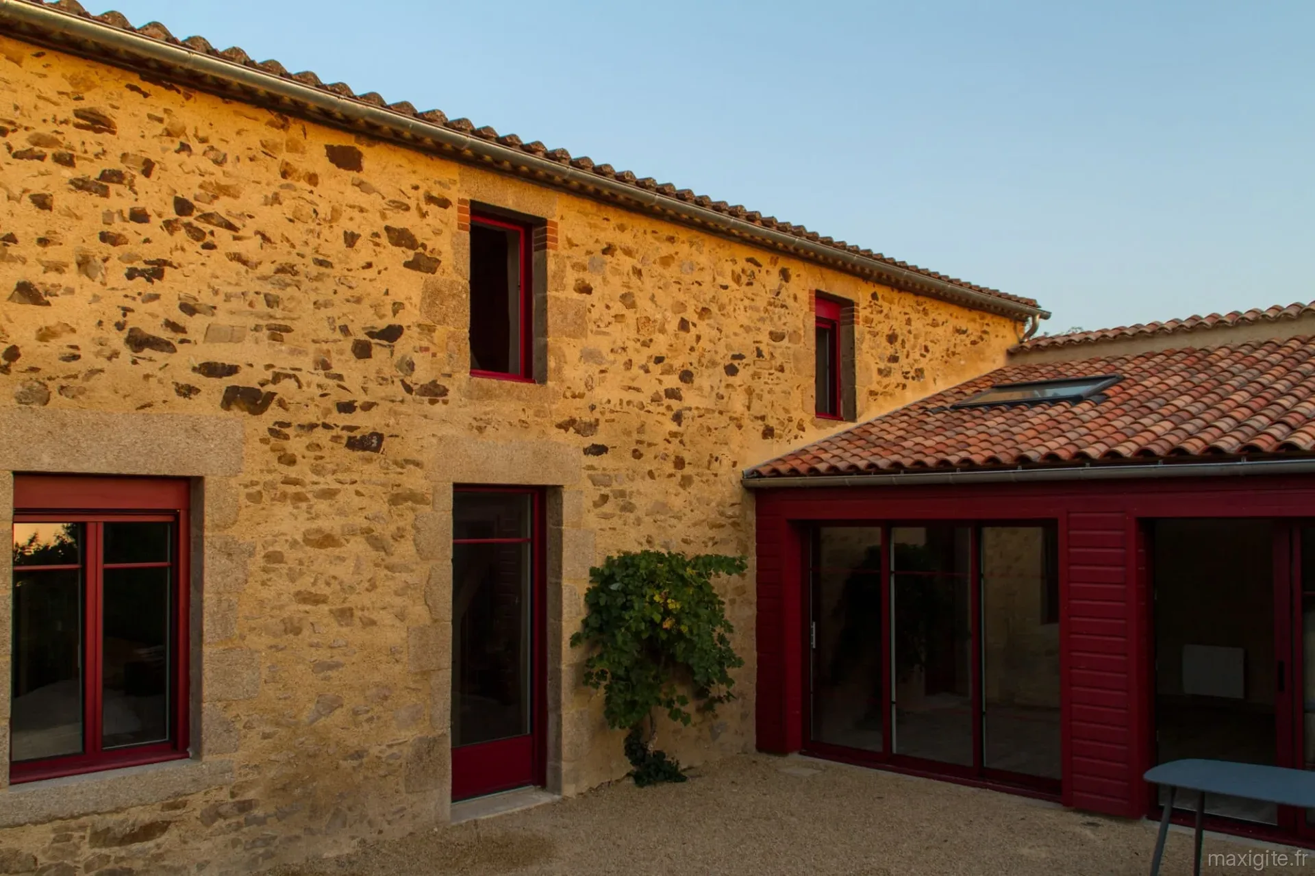 Gîte de groupe Le Puy Carmin - Gîte de groupe à Bazoges-en-Paillers — Façade en pierre du gîte avec volets rouges, terrasse et jardin fleuri, capacité 12 personnes