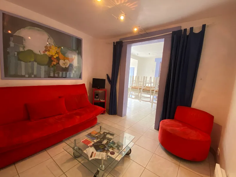 Les Gîtes du Torgan – MassacSalon avec canapé rouge et fauteuil assorti, ouvert sur la salle à manger