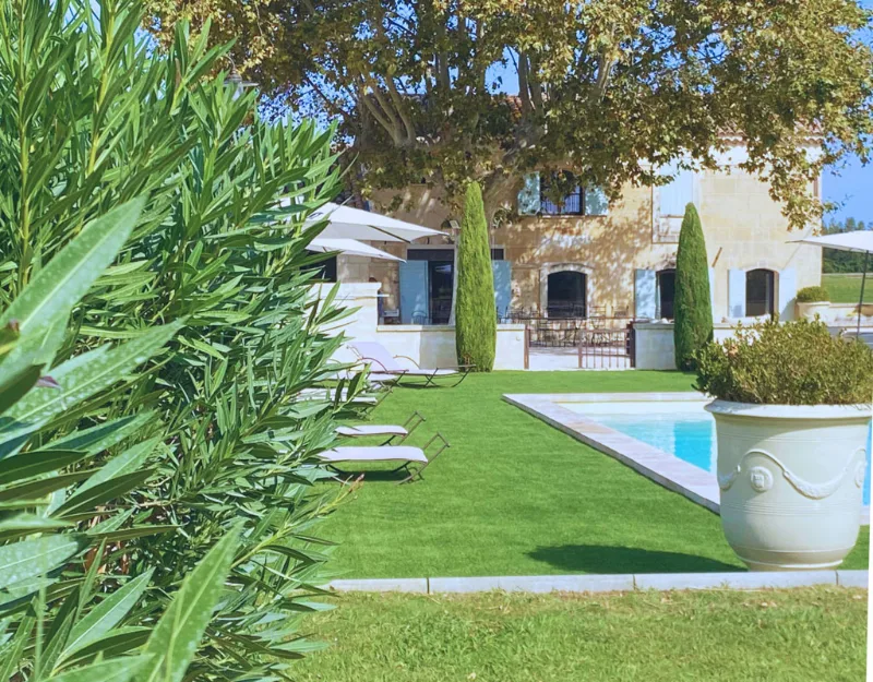 Façade en pierre du mas avec piscine, palmiers et jardin arboré
