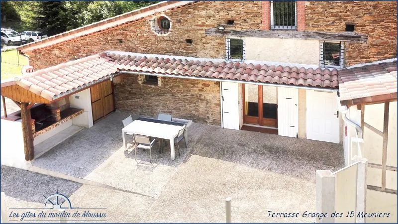 Terrasse couverte avec table en bois et barbecue en pierre