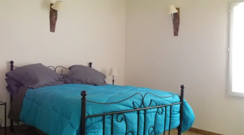 Chambre double avec couvre-lit turquoise et lampes murales en fer forgé