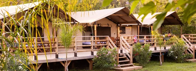Rangée de lodges tentes en bois sur pilotis, entourés de végétation méditerranéenne