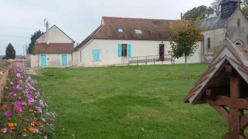 Grand jardin clos avec pelouse, parterre de fleurs et vue sur l'église voisine du village