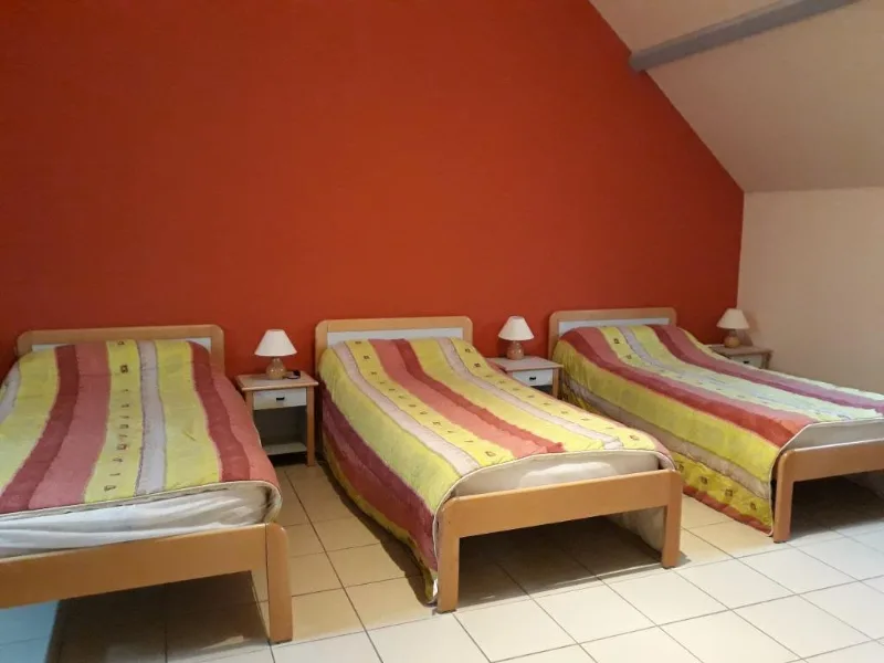 Chambre lumineuse sous les combles avec trois lits simples et murs orangés