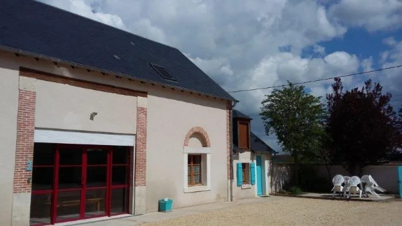 Façade du bâtiment annexe avec porte-fenêtre rouge et coin détente extérieur ombragé