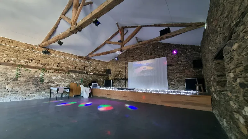 Salle en pierre voûtée avec charpente bois, aménagée pour les soirées festives et animations