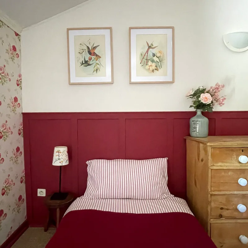 Chambre chaleureuse aux tons rouges avec lit simple, gravures et commode ancienne
