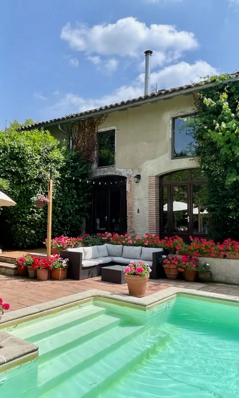 Façade en pierre côté jardin avec piscine, mobilier d'extérieur et parterres de fleurs