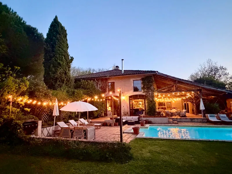 Façade de la maison illuminée le soir avec terrasse, guirlandes lumineuses et piscine