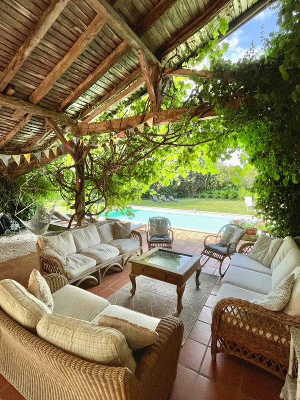 Terrasse couverte avec salon en osier et vue directe sur la piscine et le jardin