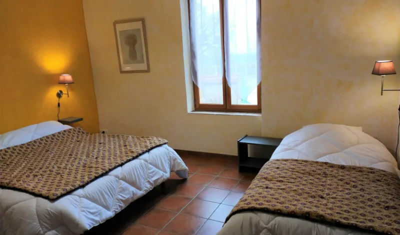 Chambre lumineuse avec deux lits doubles, murs jaune ocre et sol en tomettes