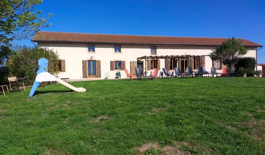 Gîte de groupe Le Bois Rond à Céron — Façade en pierre de la longère du 19e siècle avec terrasse ombragée sous pergola et jardin, capacité 15 personnes