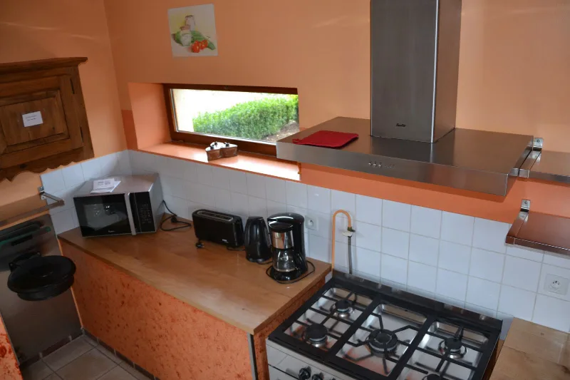 Cuisine équipée avec cuisinière à gaz, hotte inox et espace de préparation carrelé