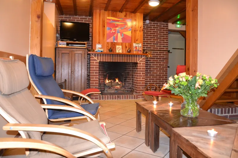 Salon chaleureux avec cheminée en briques, fauteuils confortables et poutres apparentes