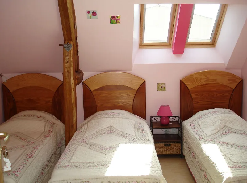 Chambre sous les toits avec trois lits simples, poutre en bois et velux