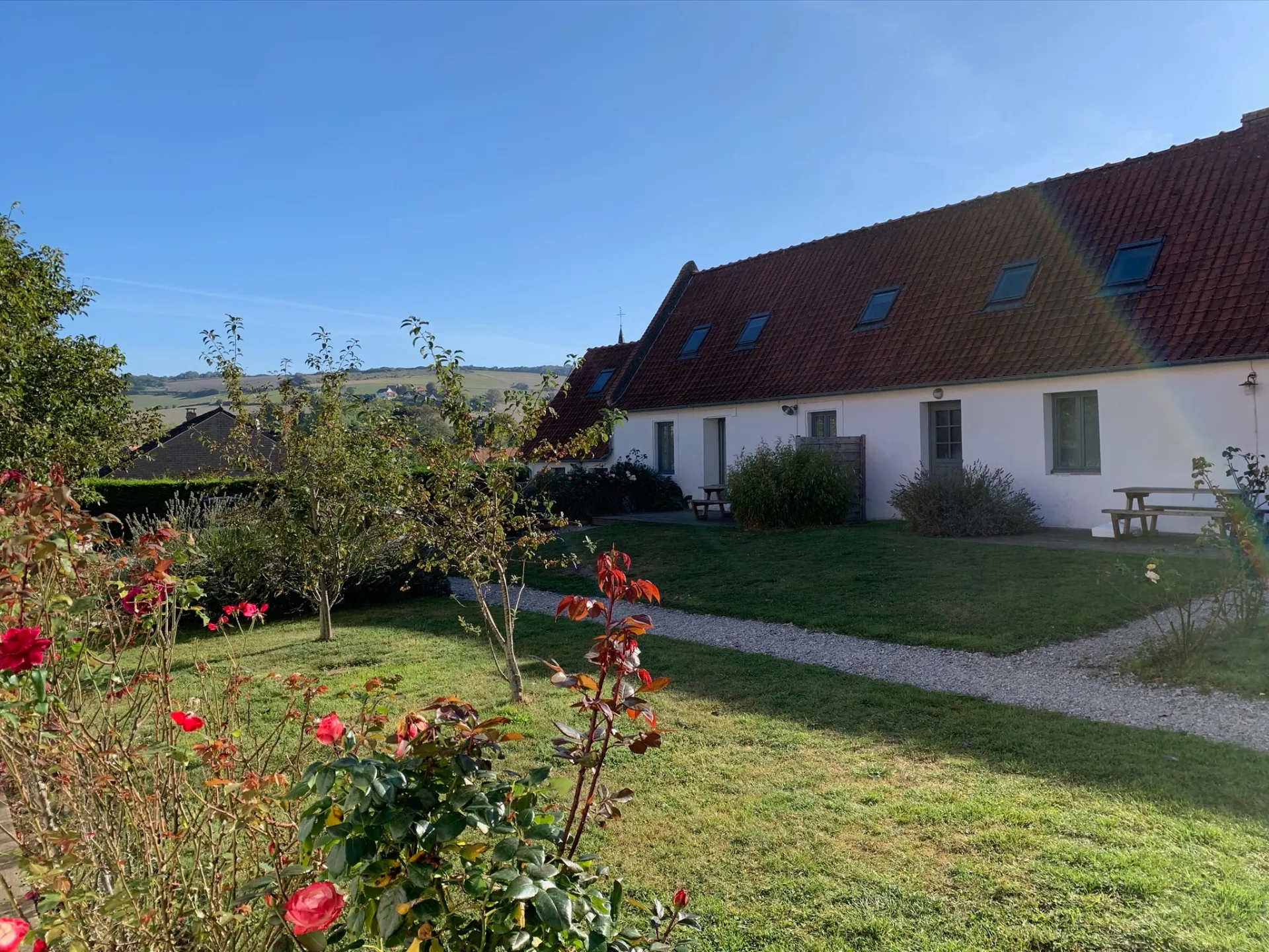 Gîte de groupe Les Gîtes du Mont de Couple à Hervelinghen — Façade en pierre du gîte avec jardin verdoyant et ciel dégagé au-dessus des toits, capacité 34 personnes
