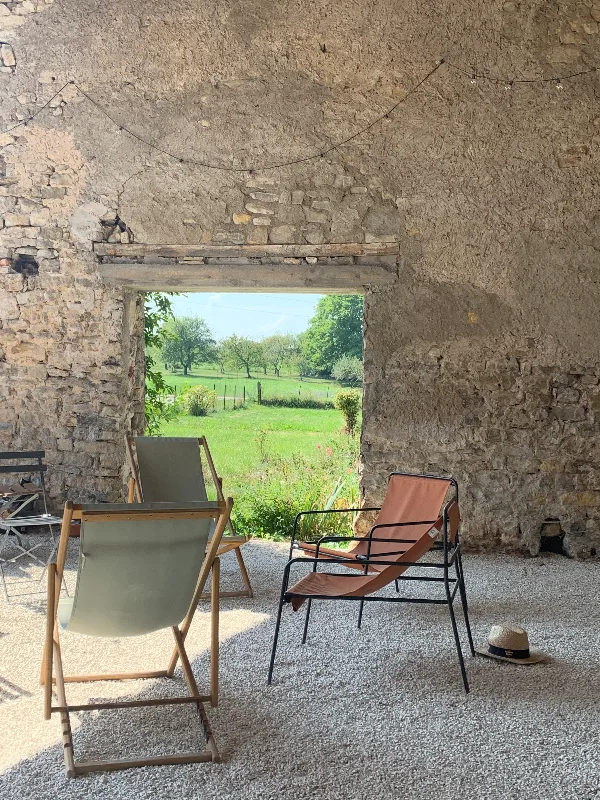 Façade en pierre du Clos des Maix vue à travers une ouverture voûtée, jardin verdoyant et chaises longues