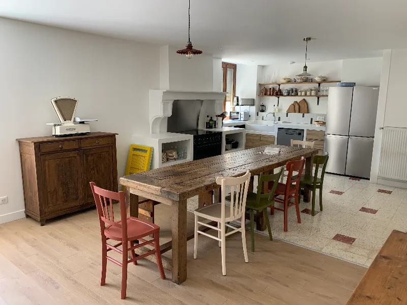 Cuisine et salle à manger conviviale avec grande table en bois massif, cheminée ancienne et chaises colorées