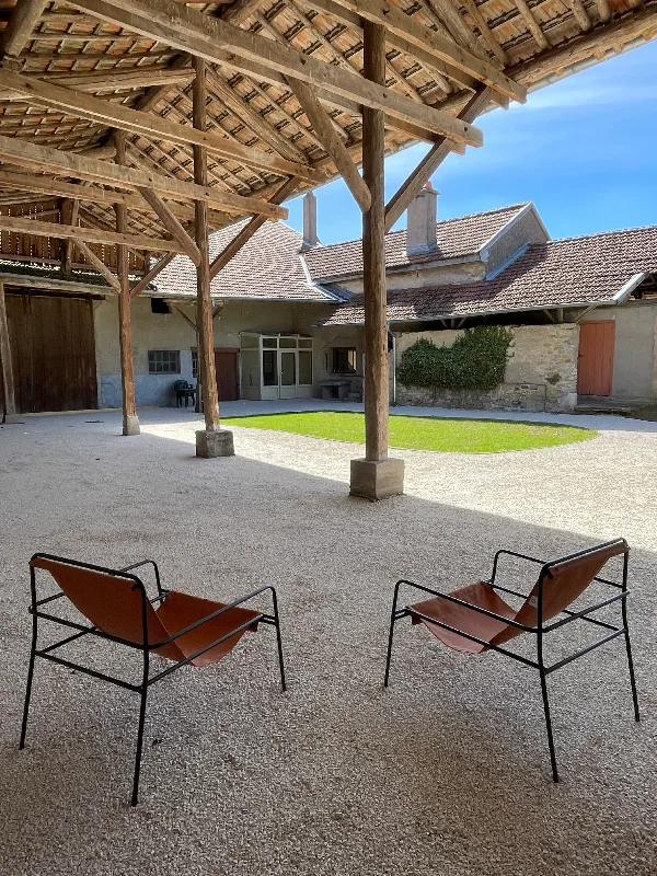 Cour extérieure ombragée avec table et chaises en toile, façades en pierre et toits en tuiles du hameau