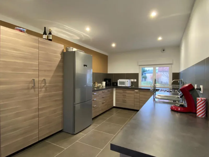 Cuisine équipée avec grand réfrigérateur inox, plan de travail en bois et fenêtre sur le jardin