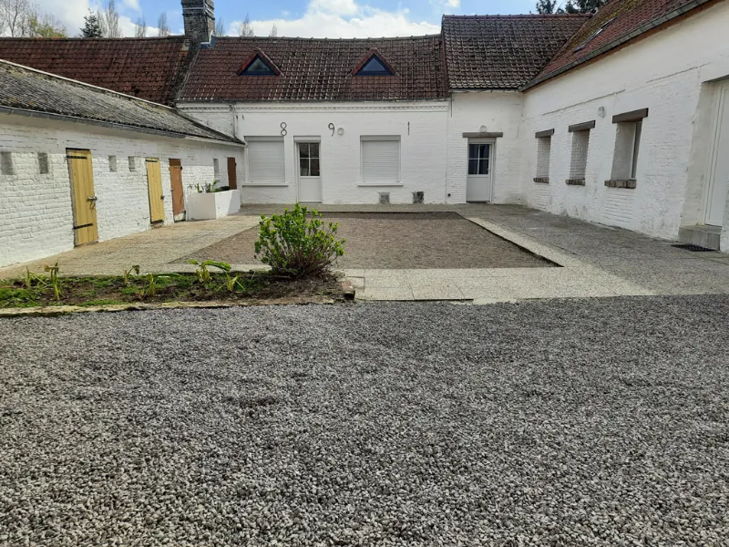 Cour intérieure pavée avec véritable terrain de pétanque entre les bâtiments blancs de la fermette