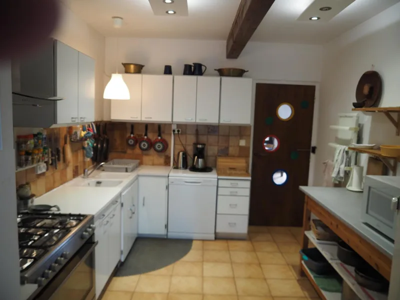 Cuisine équipée avec plaques de cuisson, ustensiles suspendus et poutre apparente au plafond