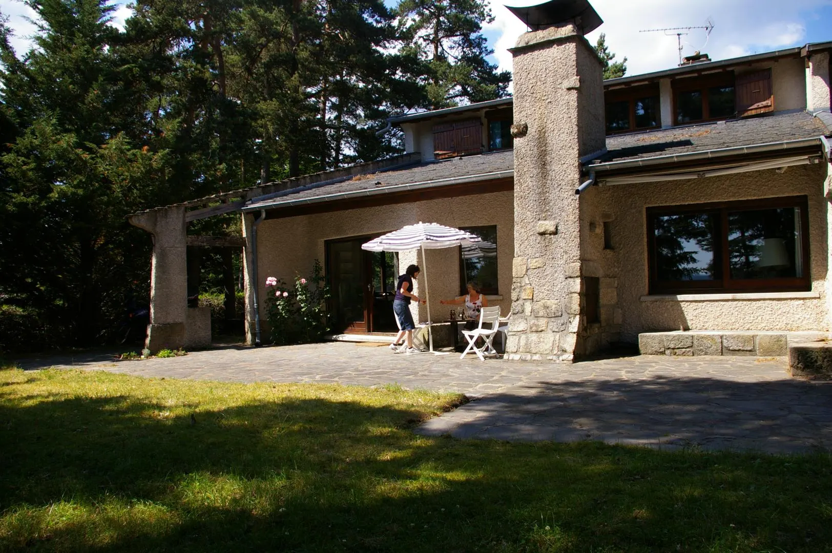 Gîte de groupe Gîte du Haut Lignon à Le Chambon-sur-Lignon — Façade en pierre de la maison d'architecte avec terrasse ombragée et cheminée en granit, capacité 15 personnes