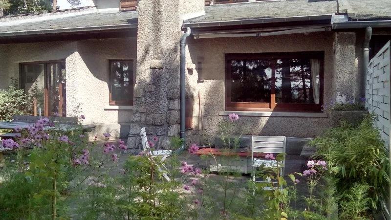 Terrasse fleurie de cosmos avec chaises de jardin, façade en pierre et grandes fenêtres