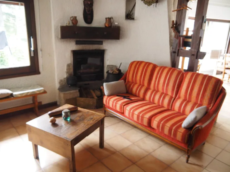 Salon chaleureux avec cheminée en pierre, canapé rayé orange et banquette en bois