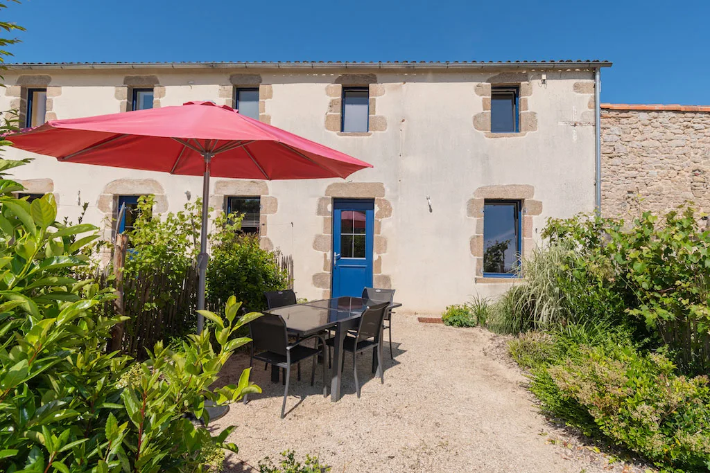 Gîte de groupe Le Logis de Concise à Les Herbiers — Façade du Logis de Concise avec terrasse ombragée, table extérieure et parasol rouge, capacité 30 personnes