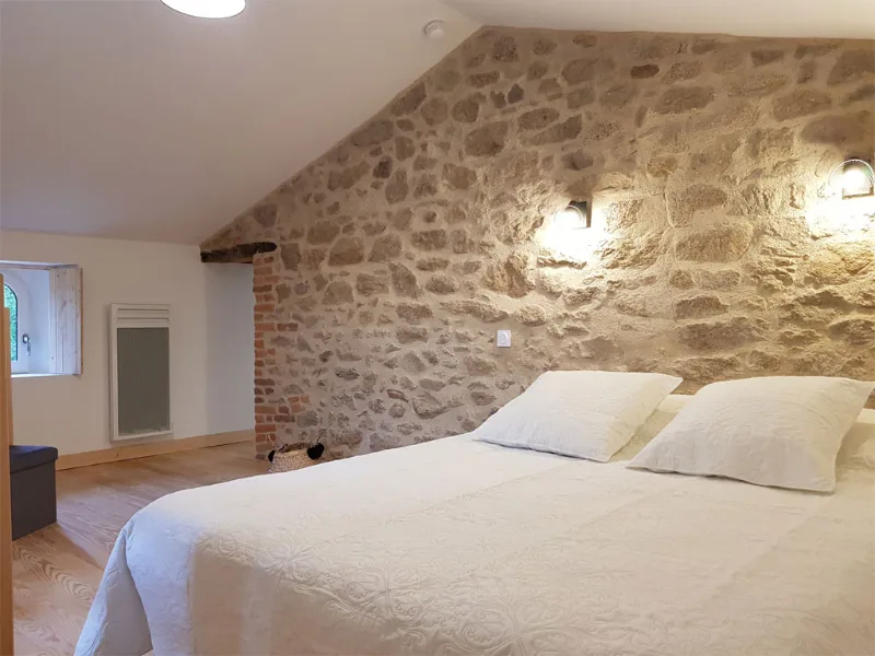 Chambre lumineuse avec mur en pierre apparente et lit double à couette blanche
