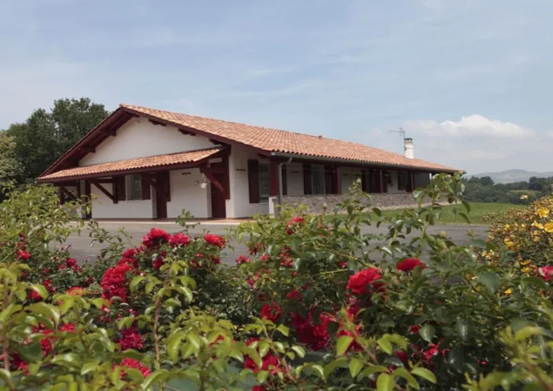 Vue d'ensemble du gîte basque entouré de rosiers rouges et de son grand terrain