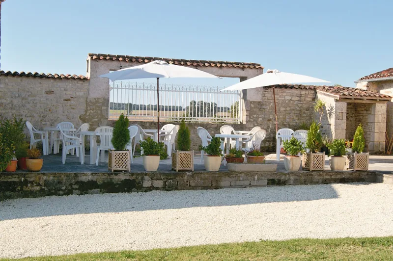 Terrasse en pierre avec parasols blancs, tables et chaises pour les repas en groupe