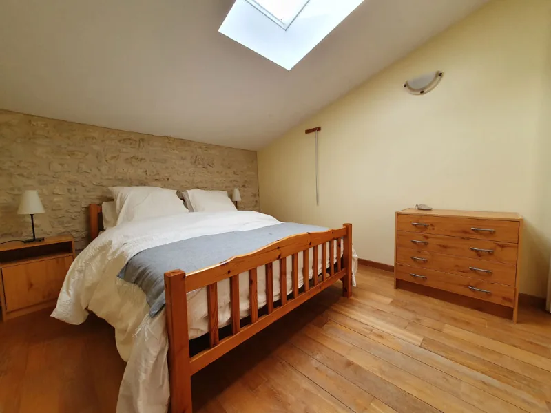 Chambre mansardée avec mur en pierre apparente, lit double et fenêtre de toit
