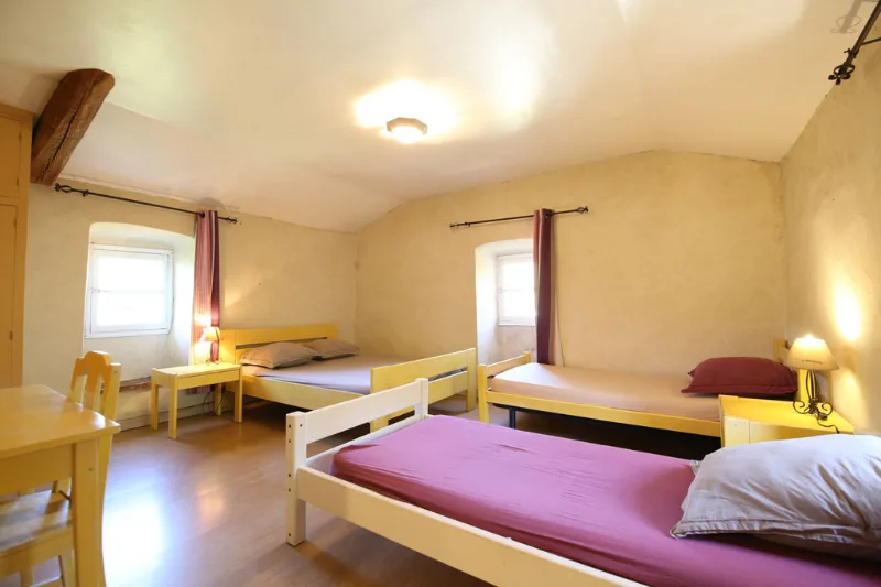 Chambre collective en pierre avec plusieurs lits simples aux rideaux bordeaux