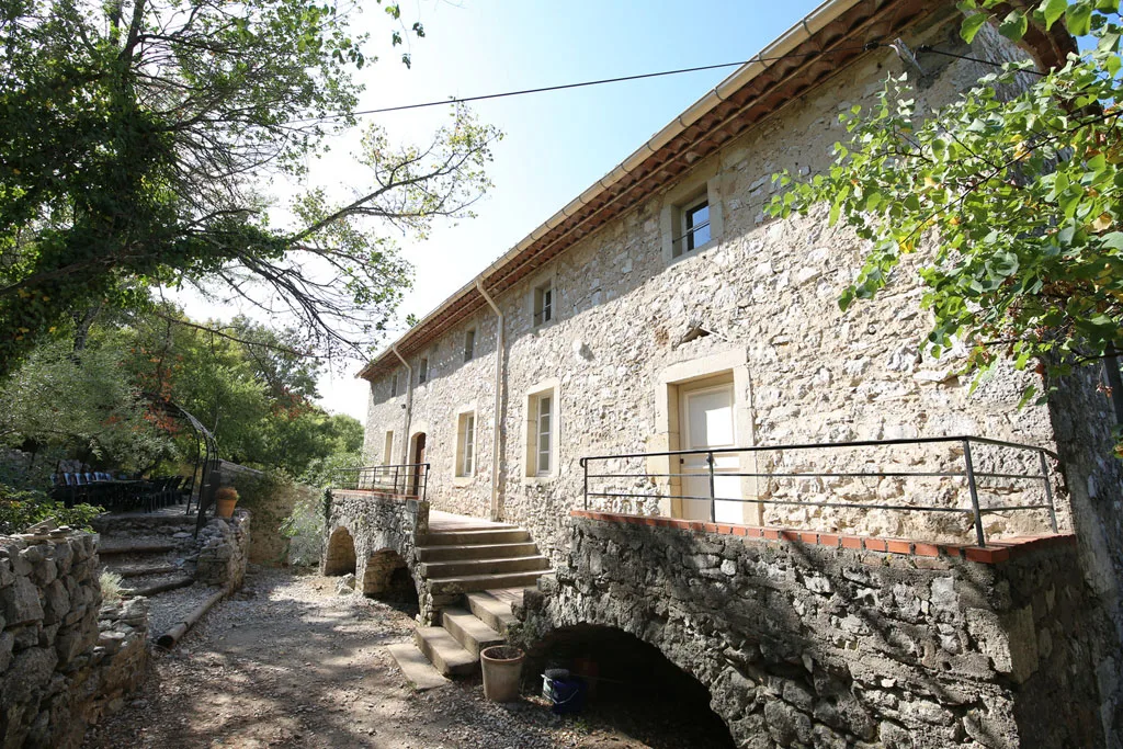 Gîte de groupe Mas du Granzon à Banne — Façade en pierre du mas ardéchois avec terrasse en pierre et escalier extérieur, capacité 23 personnes