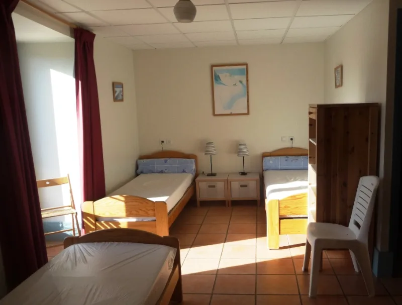 Chambre lumineuse avec lits simples en bois et grande armoire, sol carrelé