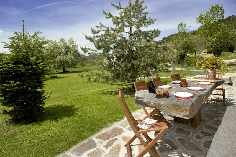 Terrasse en pierre avec grande table dressée et vue sur les prairies et collines boisées