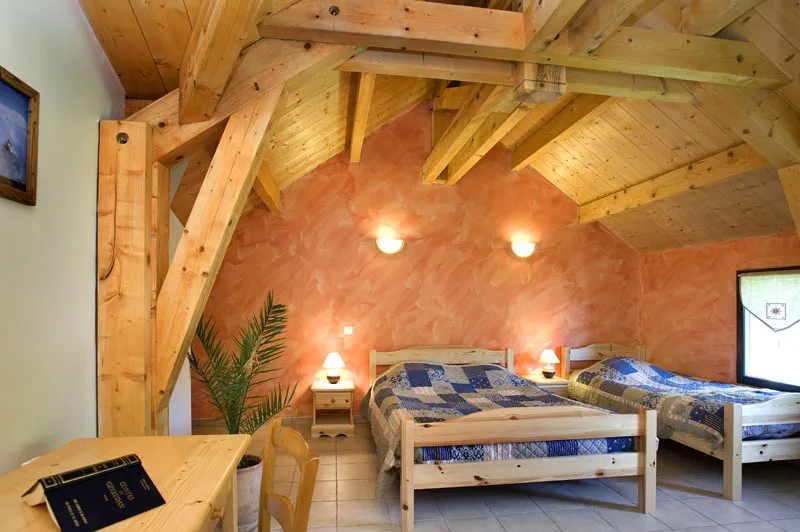 Chambre mansardée sous charpente en bois avec deux lits doubles en patchwork bleu