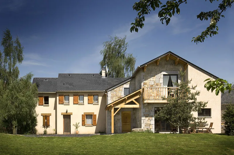 Façade du gîte Le Gévaudan avec balcon en bois et pierre, ciel bleu et grand jardin