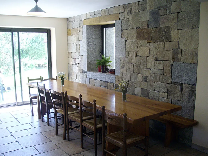 Salle à manger avec longue table en bois massif et mur en pierres apparentes