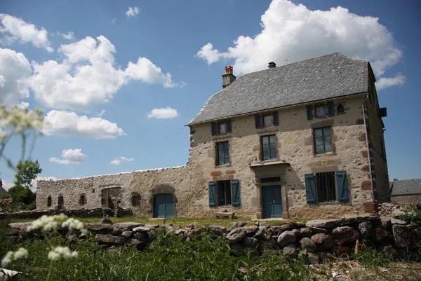 Façade en pierre de Fortuniès avec toit d'ardoises et volets bleus, ciel dégagé
