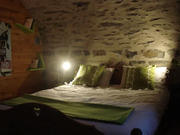 Chambre douillette avec lit double, coussins verts et mur en pierre apparente