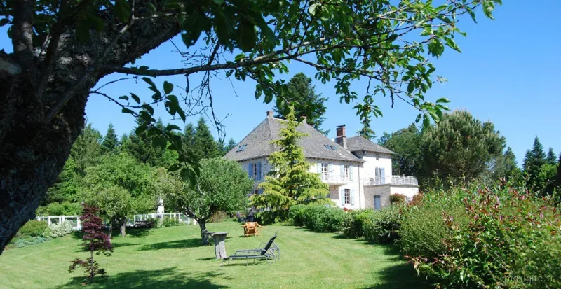 Façade en pierre de la maison de maître entourée d'un grand parc arboré et fleuri